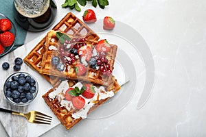 Board with delicious Belgian waffles, berries and whipped cream on light marble table, flat lay. Space for text