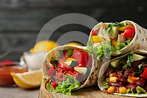 Board with delicious meat tortilla wraps on table against black background, closeup