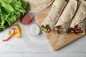 Board with delicious meat tortilla wraps on white wooden table