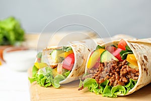 Board with delicious meat tortilla wraps on white wooden table
