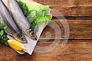 Board with delicious salted herrings, lemon and herbs on wooden table, top view. Space for text