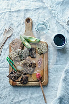 A board with different vegan snacks together with honey, glass of water and wooden forks lieing on rough linnen fabric