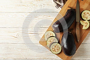 Board with fresh raw eggplants on white wooden background