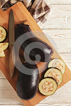 Board with fresh raw eggplants on white wooden background