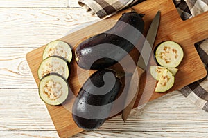 Board with fresh raw eggplants on white wooden background