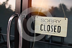 The board hung in front of the glass door of the coffee shop had a  message sorry and closed. Light from the soft sun in the