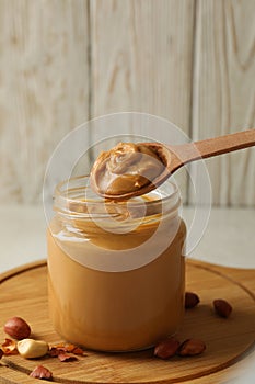 Board with peanut, spoon and jar with peanut butter on white table