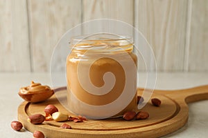 Board with peanut, spoon and jar with peanut butter on white table