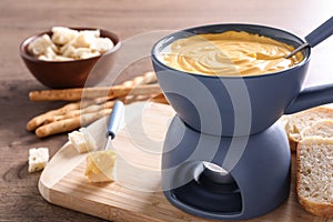 Board with pot of cheese fondue, bread and fork on table, space for