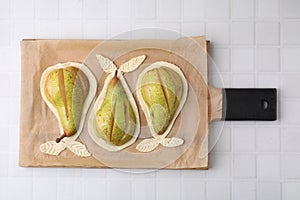 Board with raw dough and fresh pears on white tiled table, top view