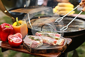 Board with raw meat and vegetables near barbecue grill