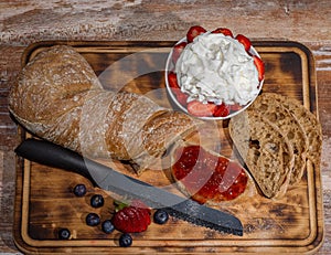 Board with slices of bread and delicious strawberry jam on wooden table