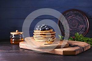 Board with tasty pancakes, honey dipper and blueberries on wooden table