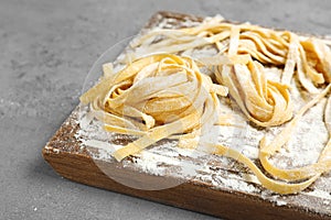 Board with uncooked egg noodles and flour on grey table