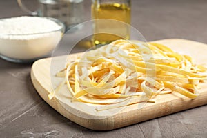 Board with uncooked egg noodles on grey table,