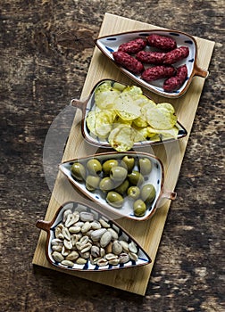 Board with a variety of snacks for wine, beer - spicy sausages, potato chips, olives, pistachios on a wooden background, top view