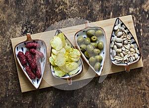 Board with a variety of snacks for wine, beer - spicy sausages, potato chips, olives, pistachios on a wooden background, top view