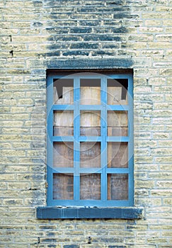 Boarded up blue window in a derelict house with dirty brick wall