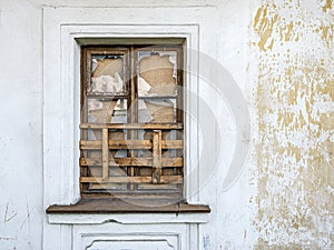 Boarded up window with broken glass on weathered plaster wall