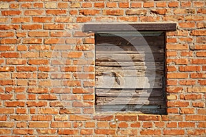 Boarded up with wooden planks window opening in an old red brick wall