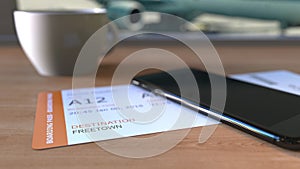 Boarding pass to Freetown and smartphone on the table in airport while travelling to Sierra Leone