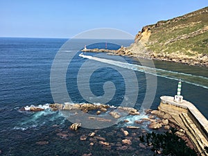 Boat acrossing the Cantabric sea with a lighthouse and the mountains