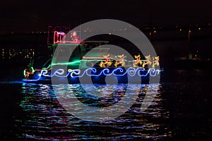 Boat Adorned with Christmas Holiday Lights, Santa Claus Sleigh and Reindeer and Reflection in the Water.