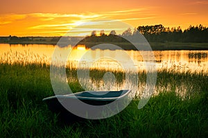 Boat on bank of river at sunset in grass