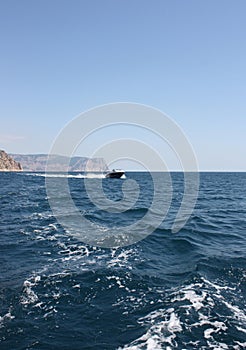 A boat in the blue sea against the background of a large rock.