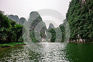 Boat cave tour in Trang An Scenic Landscape formed by karst towers and plants along the river (UNESCO World Heritage Site). It's