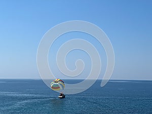 Boat with a colored parachute floats on the sea against a blue sky