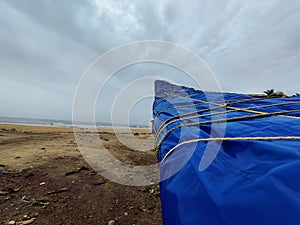 A boat covered with plastic sheets placed on the beach near the sea under the sky