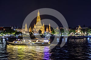Boat cruises along river past Wat Arun at twilight, Bangkok, Thailand