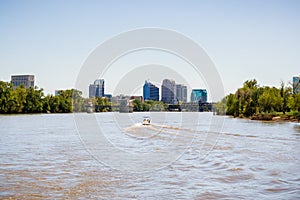 Boat cruising on the muddy looking water of Sacramento river; the City`s downtown skyline in the background; California