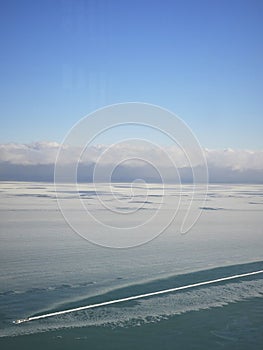 Boat cutting through sea foam. Sky meets ocean in horizon.