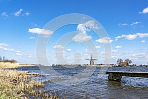 A boat dock in the rough water of lake De Rottemeren with the windmill De Korenmolen in the background on a sunny but stormy day photo