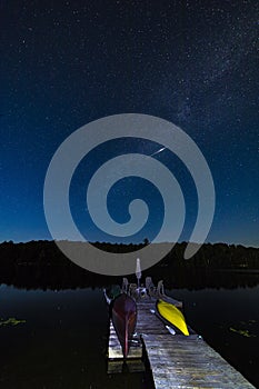 Boat dock under a starry sky as meteor streaks across the Milky