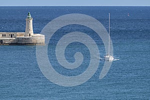 A boat enters the Grand Harbour of Valletta with the St. Elmo breakwater lighthouse in the background