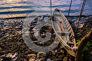 A boat and evening tide on messy riverbank at sunset