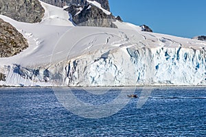 Boat full of tourists passing by the huge glacier in the bay near Cuverville island, Antarctic peninsula