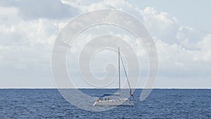 Boat with furled sails sailing across blue sea under cloudy sky, recreation