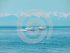 The boat at high speed goes along Lake Baikal against the backdrop of snow-capped mountains