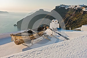 Boat on a house roof at sunset in front of Skaros rock at Imerovigli village, Santorini island