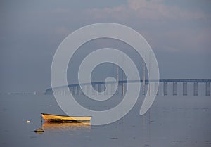 A boat is left lonely in the sea close to the shore while the fog is slowly lifting and revealing the Ã–resund bridge in the