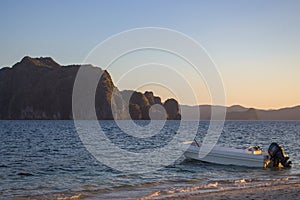 Boat near coast with islands and mountains on horizon. Beautiful calm sunset on beach in Philippines. Evening seascape panorama.