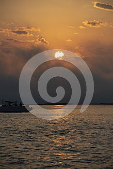 Boat on ocean, Bright sun in an orange sky with dark clouds at sunset