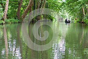 Boat with people on marsh canal under big trees, France
