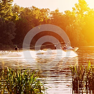 Boat pulls man water skiing on the river. Sunset. Splashes of water.