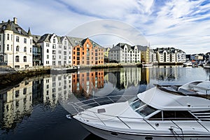 Boat on the river surrounded by colorful buildings under a cloudy sky in Alesund in Norway