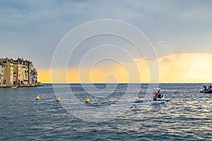 Boat sailing in the Adriatic Sea during sunset of a cloudy day with the typical croatian houses of Rovinj, Croatia, on the left